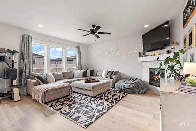 living room with ceiling fan, a fireplace, and light hardwood / wood-style floors