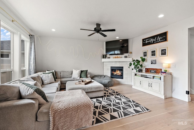 living room with ceiling fan, light wood-type flooring, and a tile fireplace