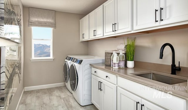 clothes washing area featuring washing machine and clothes dryer, cabinet space, light wood-style floors, a sink, and baseboards