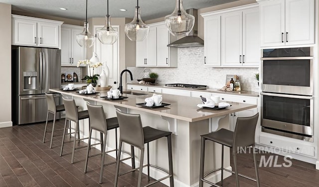 kitchen featuring dark wood finished floors, appliances with stainless steel finishes, white cabinets, a sink, and wall chimney exhaust hood