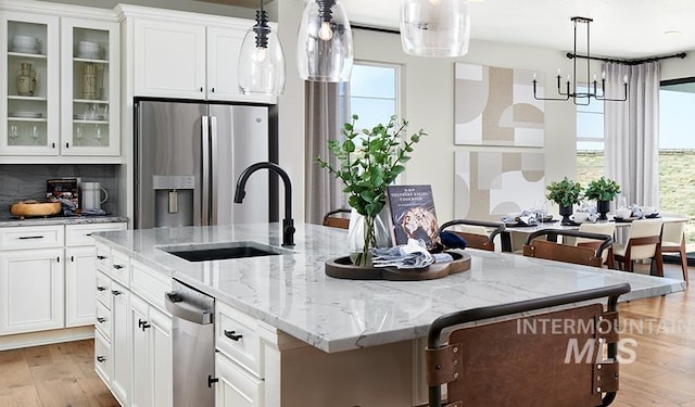 kitchen featuring a kitchen island with sink, stainless steel appliances, a sink, white cabinetry, and light wood-style floors