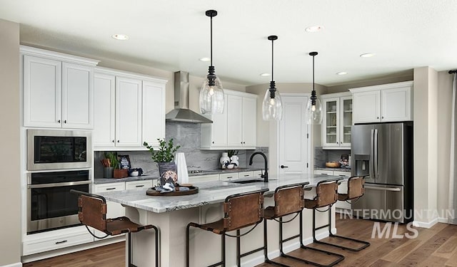 kitchen with wall chimney exhaust hood, dark wood-type flooring, stainless steel appliances, white cabinetry, and a sink