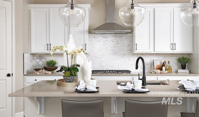 kitchen featuring wall chimney range hood, stainless steel gas cooktop, and white cabinets