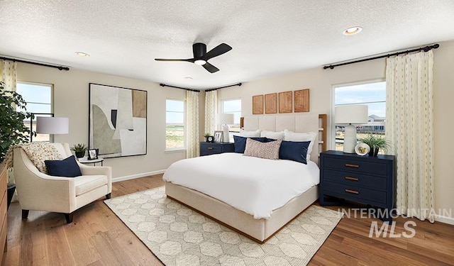 bedroom with ceiling fan, a textured ceiling, baseboards, and wood finished floors