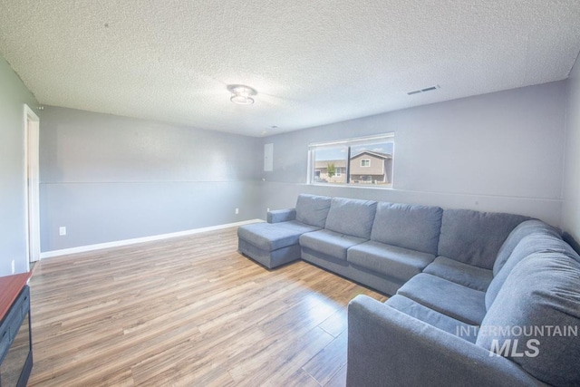 living room with baseboards, a textured ceiling, wood finished floors, and visible vents