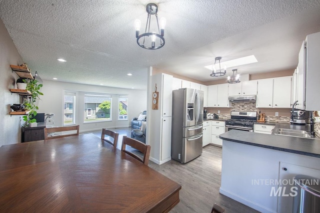 kitchen featuring open floor plan, under cabinet range hood, a sink, a notable chandelier, and stainless steel appliances