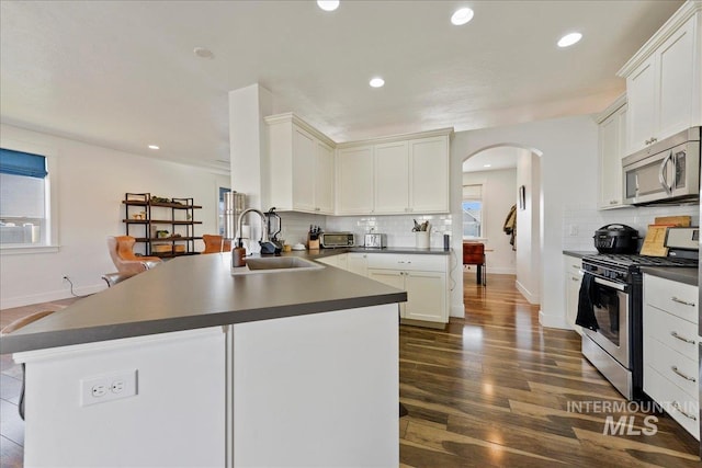 kitchen featuring arched walkways, appliances with stainless steel finishes, dark countertops, and a sink