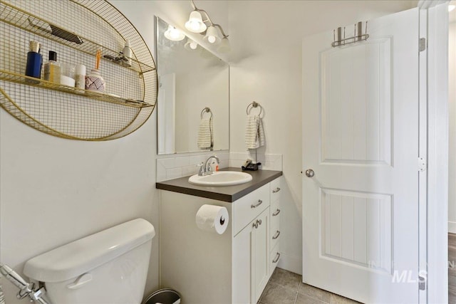 half bath featuring toilet, tile patterned flooring, backsplash, and vanity