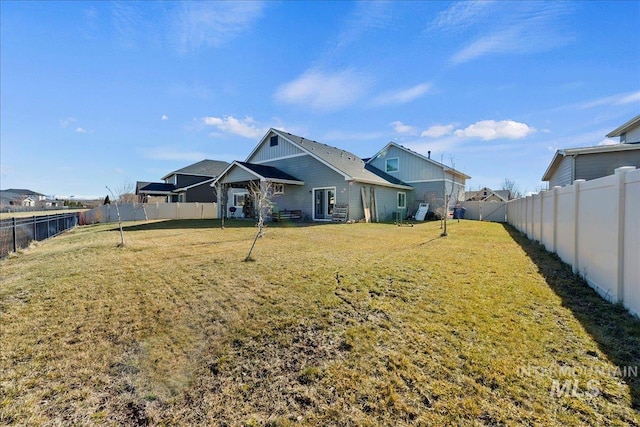 rear view of house featuring a fenced backyard and a yard