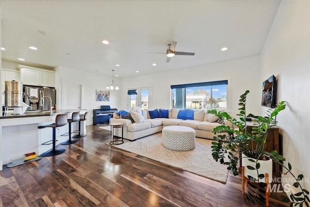 living room with dark wood-type flooring, recessed lighting, and ceiling fan with notable chandelier