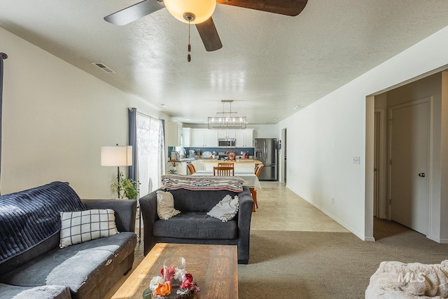 living room with a ceiling fan, baseboards, visible vents, a textured ceiling, and light colored carpet