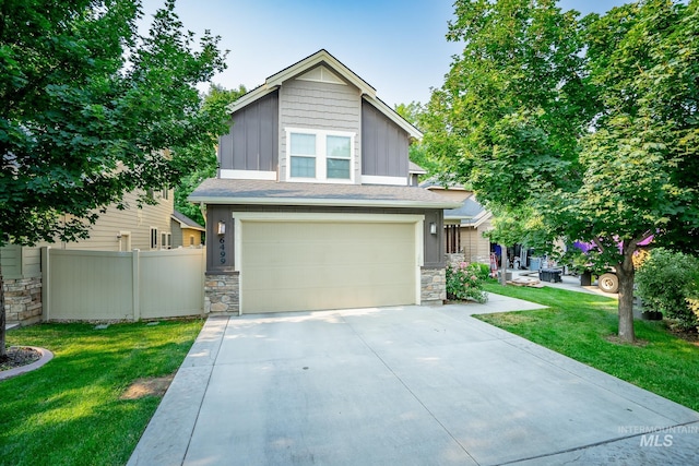 view of front of house featuring driveway, stone siding, fence, a front lawn, and board and batten siding