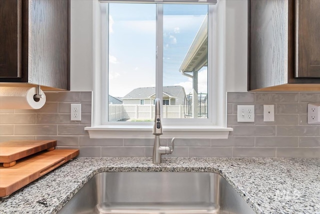 interior details with dark brown cabinetry, light stone countertops, a sink, and tasteful backsplash