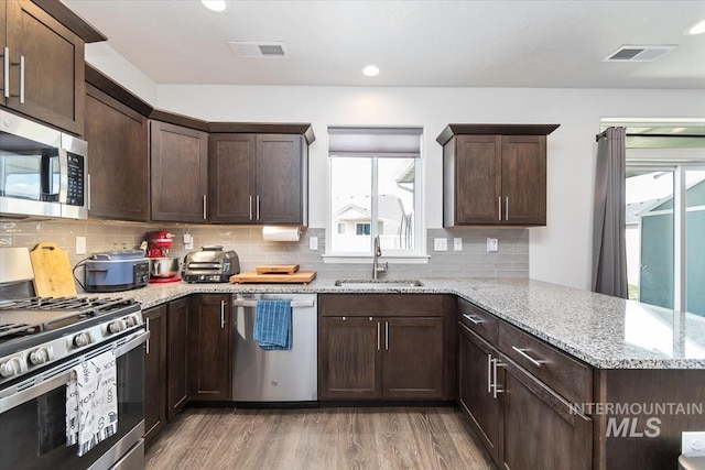 kitchen with stainless steel appliances, a peninsula, a sink, light wood-type flooring, and visible vents