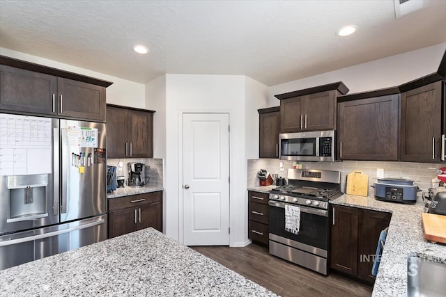 kitchen featuring stainless steel appliances, dark brown cabinetry, light stone counters, and dark wood-style flooring
