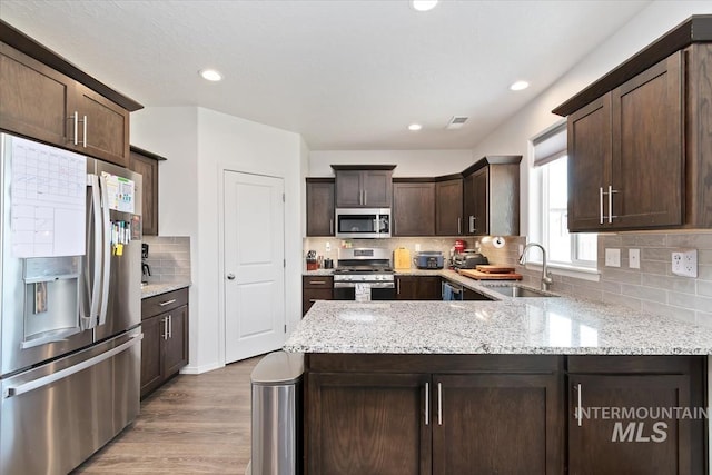 kitchen with stainless steel appliances, a sink, tasteful backsplash, dark brown cabinets, and wood finished floors