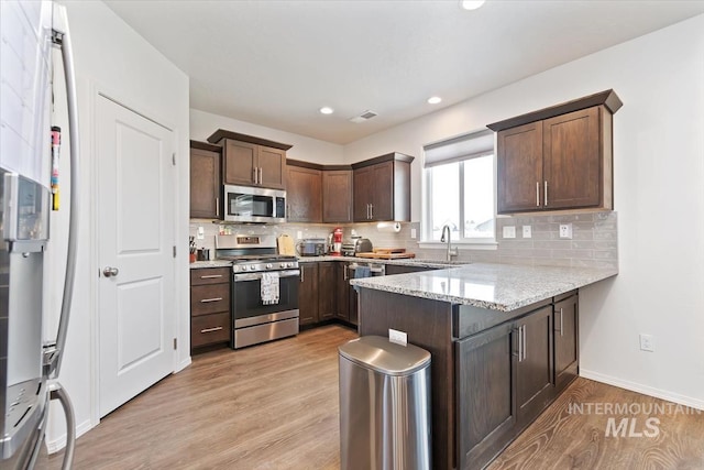 kitchen featuring light stone counters, visible vents, a sink, a peninsula, and appliances with stainless steel finishes