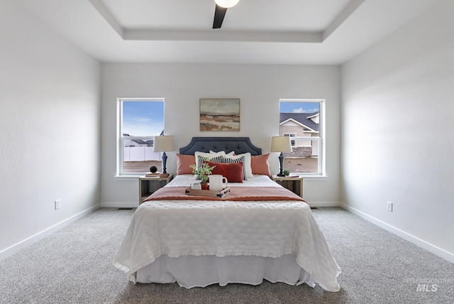 carpeted bedroom with a raised ceiling and ceiling fan