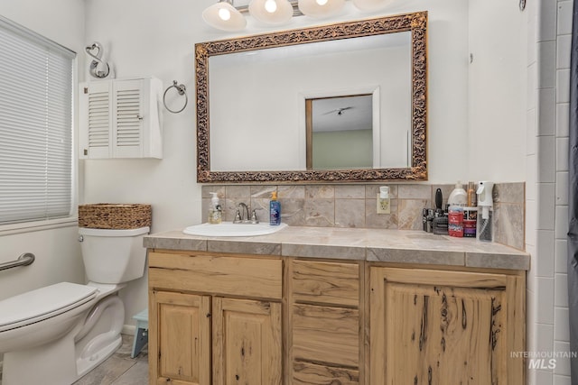 bathroom with double vanity, tasteful backsplash, a sink, and toilet