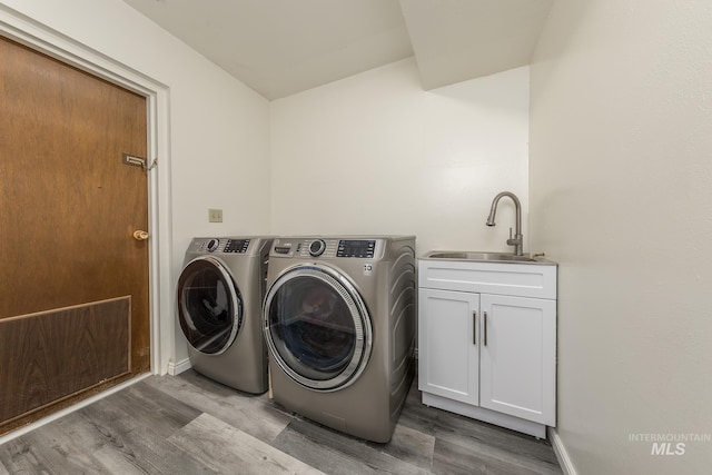 laundry area featuring washing machine and clothes dryer, cabinet space, a sink, wood finished floors, and baseboards