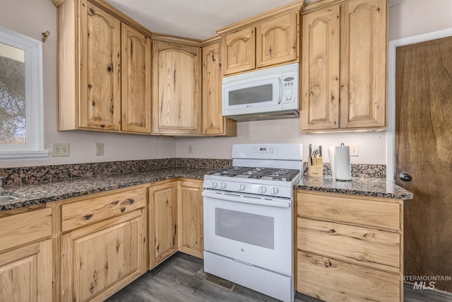 kitchen with white appliances, dark stone countertops, and light brown cabinetry