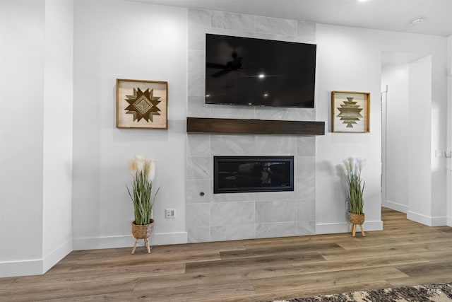 unfurnished living room with wood finished floors, a tile fireplace, and baseboards