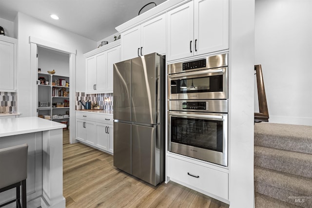 kitchen featuring appliances with stainless steel finishes, light wood finished floors, light countertops, white cabinetry, and recessed lighting
