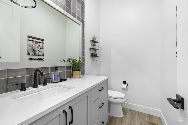 bathroom featuring wood finished floors, toilet, vanity, baseboards, and tasteful backsplash