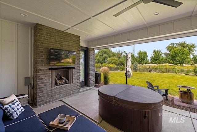 view of patio / terrace featuring an outdoor brick fireplace, a hot tub, and a ceiling fan