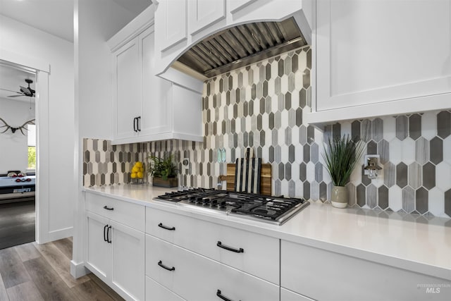 kitchen with stainless steel gas stovetop, backsplash, light countertops, white cabinetry, and wood finished floors