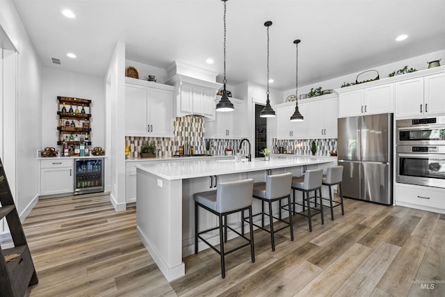 kitchen featuring appliances with stainless steel finishes, beverage cooler, light wood-style floors, decorative backsplash, and recessed lighting