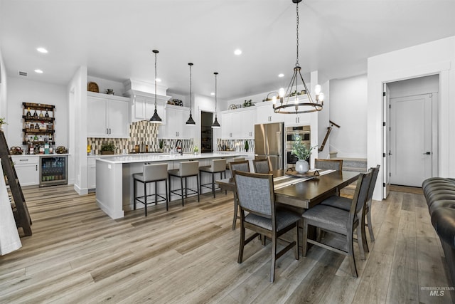 dining area featuring wine cooler, recessed lighting, light wood-type flooring, a chandelier, and stairway