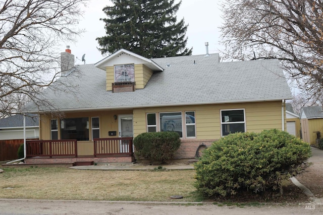 view of front of home featuring a front yard, covered porch, roof with shingles, and a chimney