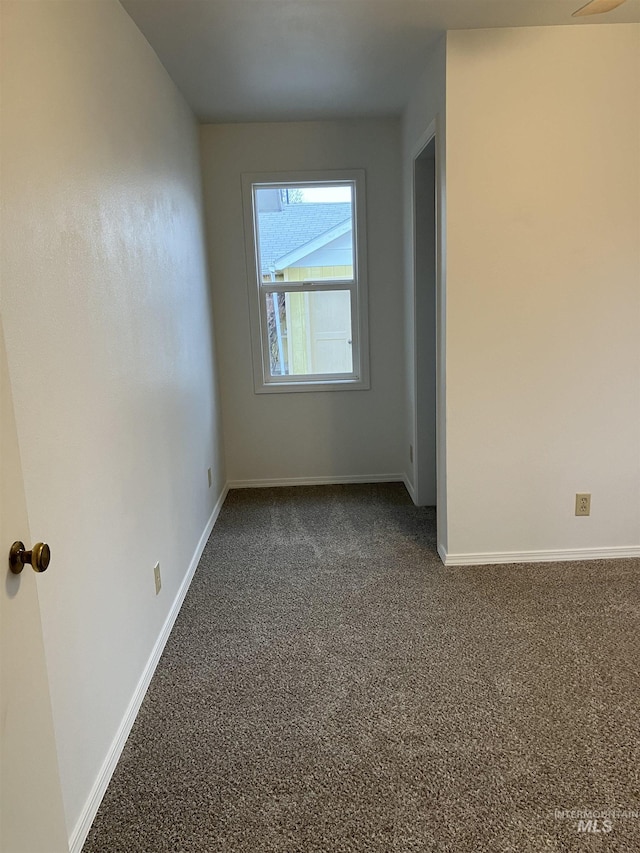 spare room with dark colored carpet and baseboards