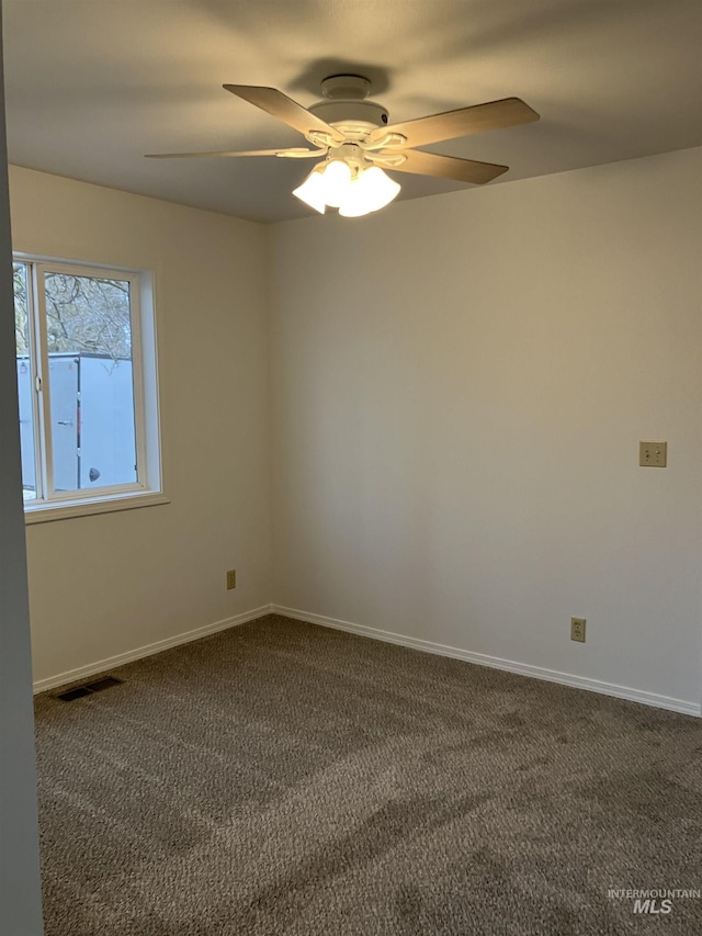 empty room with visible vents, dark carpet, baseboards, and a ceiling fan