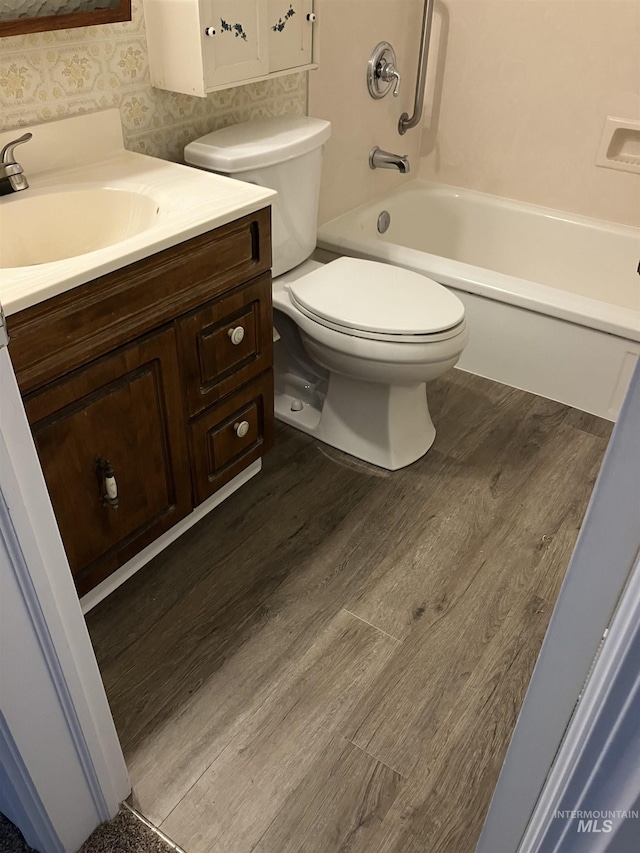 bathroom with tub / shower combination, wallpapered walls, toilet, wood finished floors, and vanity