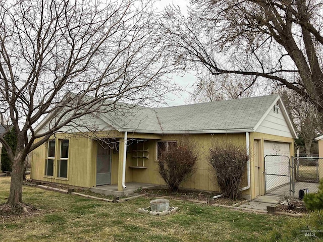 view of home's exterior featuring a gate, roof with shingles, a fire pit, a garage, and a lawn