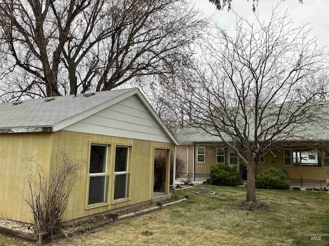 rear view of property featuring a lawn and roof with shingles