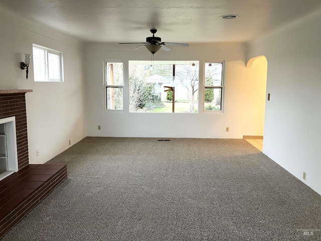 unfurnished living room featuring visible vents, a ceiling fan, arched walkways, carpet, and a fireplace