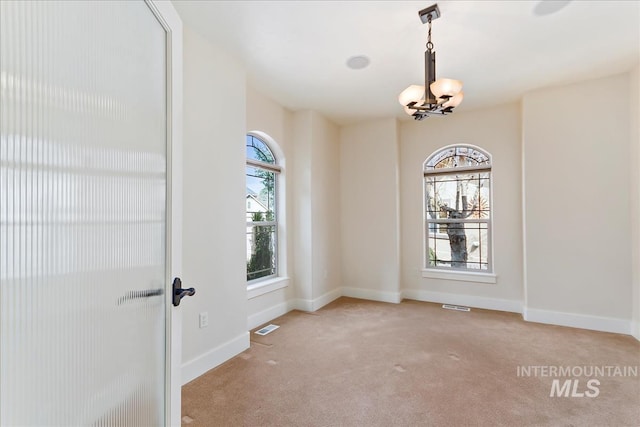 carpeted spare room with visible vents, baseboards, and a chandelier
