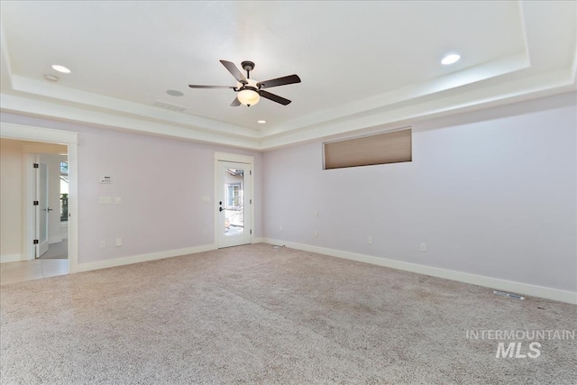 carpeted spare room with visible vents, ceiling fan, baseboards, and a tray ceiling