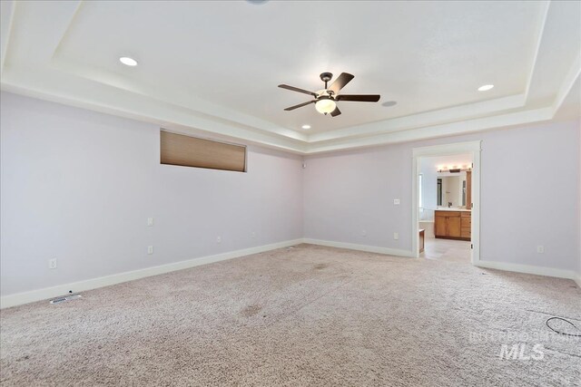 spare room with light carpet, a raised ceiling, recessed lighting, baseboards, and ceiling fan