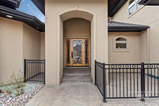 view of exterior entry with stucco siding and a shingled roof