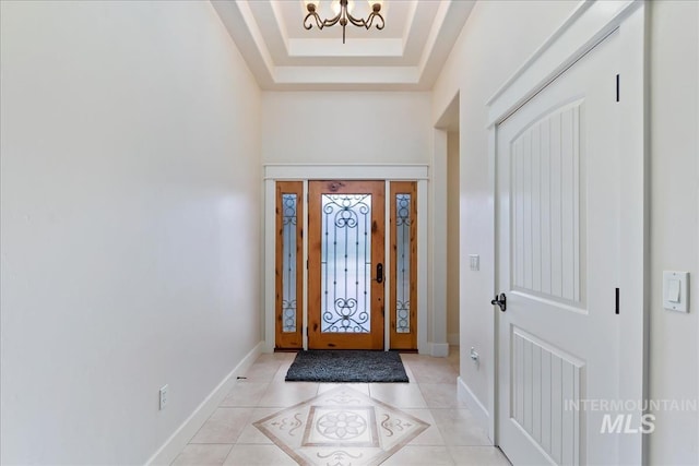 foyer with an inviting chandelier, light tile patterned floors, baseboards, and a raised ceiling