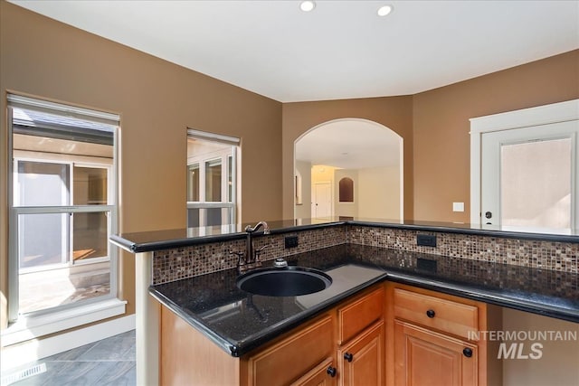 kitchen with visible vents, dark stone counters, arched walkways, a sink, and decorative backsplash