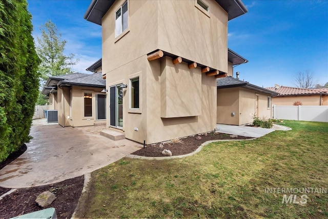 back of property with fence, a yard, a shingled roof, stucco siding, and a patio area