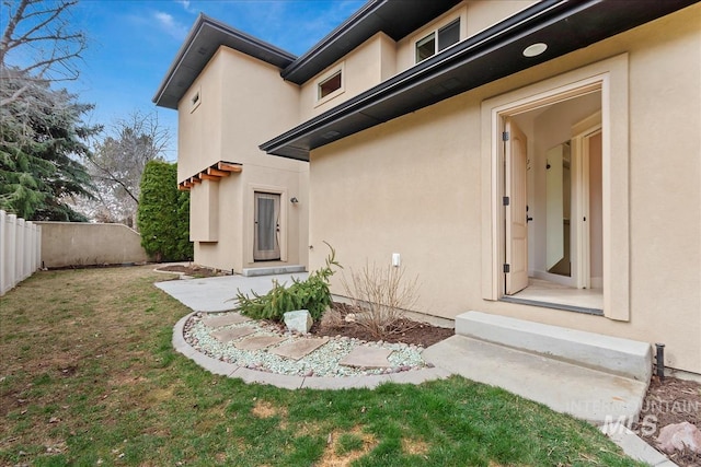 doorway to property featuring stucco siding, a lawn, and fence