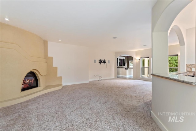 unfurnished living room featuring arched walkways, a fireplace, baseboards, and carpet floors