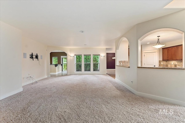unfurnished living room featuring carpet, arched walkways, and baseboards