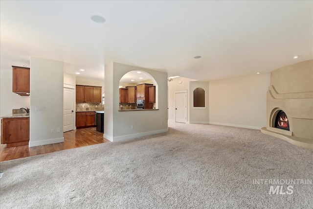 unfurnished living room with light carpet, recessed lighting, baseboards, and a sink